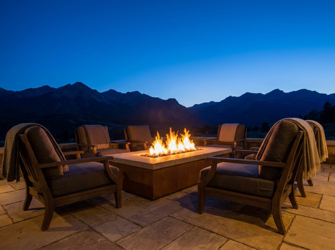 Modern gas fire pit with chairs on a stone patio at dusk with Colorado mountains behind
